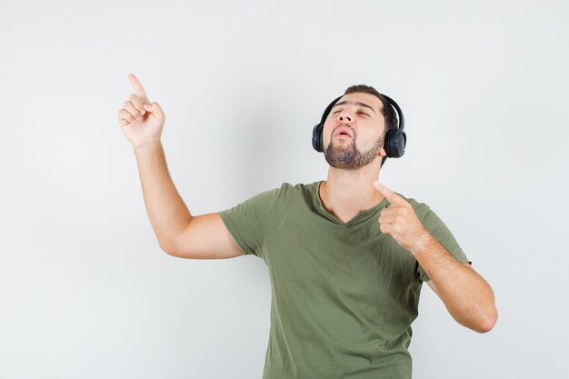 Junger Mann, der weg zeigt, während Musik in grünem T-Shirt genießt und entspannt schaut