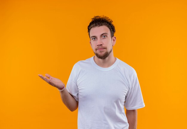 junger Mann, der weißes T-Shirt trägt, das Hand heraus an der Seite auf isolierter orange Wand hält