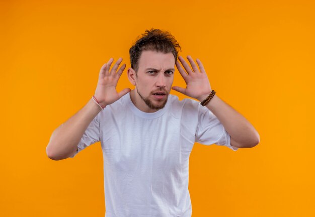 junger Mann, der weißes T-Shirt trägt, legte seine Hände um Ohren auf isolierte orange Wand
