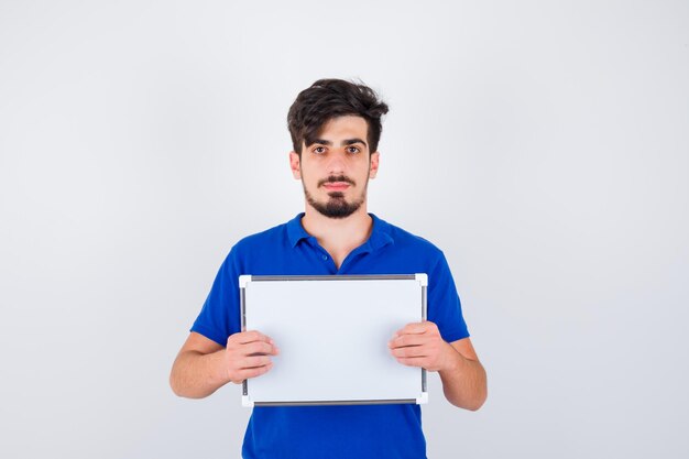 Junger Mann, der Whiteboard im blauen T-Shirt hält und ernst schaut