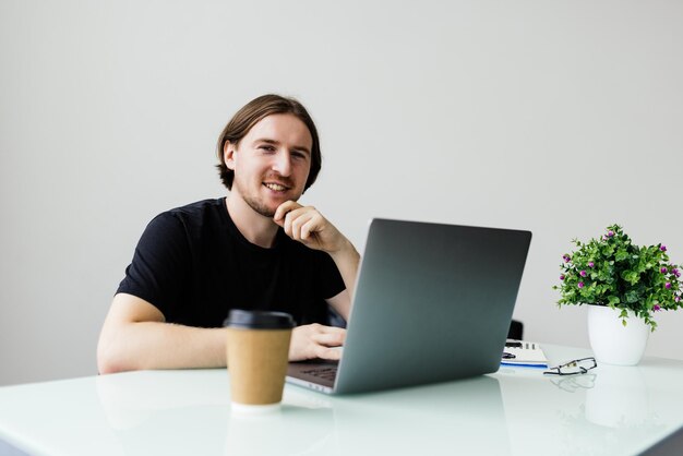 Junger Mann, der zu Hause mit Laptop und Papieren auf dem Schreibtisch arbeitet