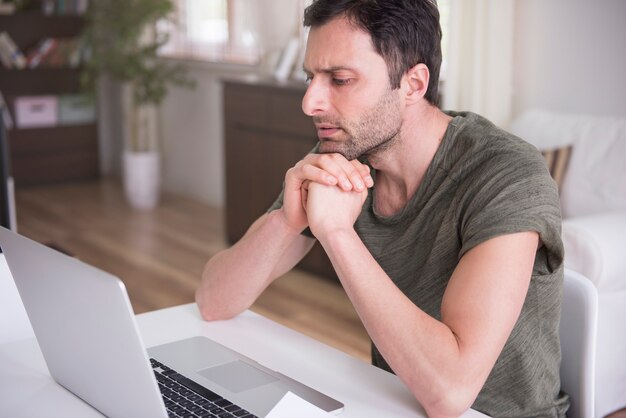 Junger Mann, der zu Hause mit seinem Laptop arbeitet