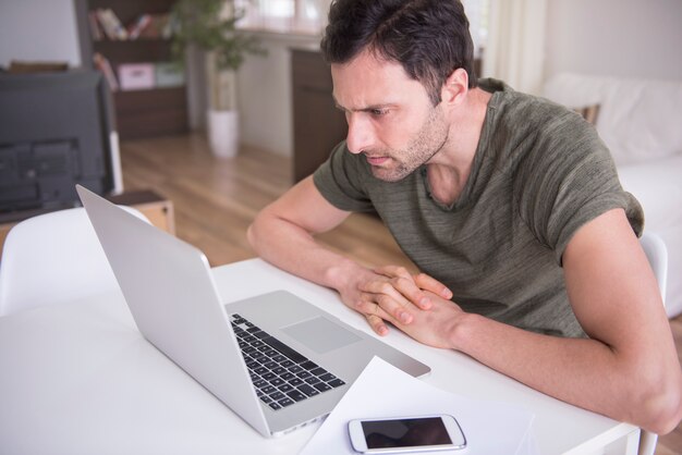 Junger Mann, der zu Hause mit seinem Laptop arbeitet