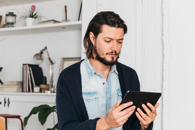 Junger Mann, der zu Hause sitzt, digitale Tablette betrachtend