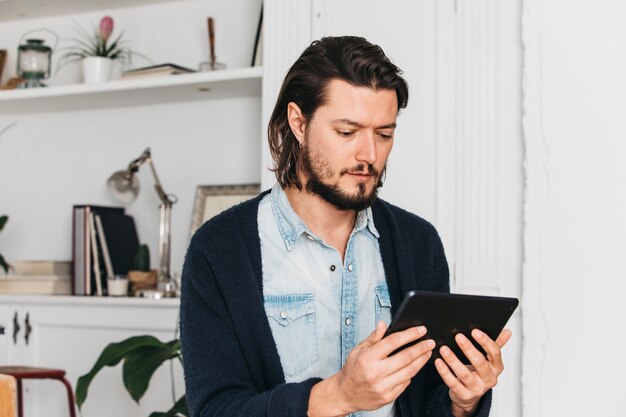 Junger Mann, der zu Hause sitzt, digitale Tablette betrachtend