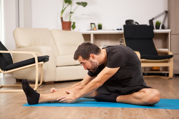 Junger Mann, der zu Hause Yoga in seinem Wohnzimmer praktiziert. Er strampelt und fühlt sich entspannt