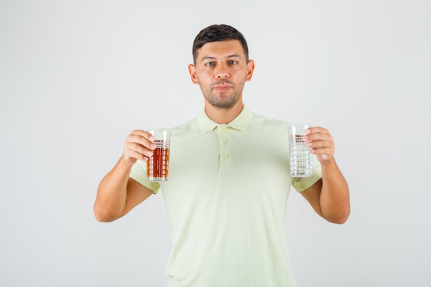 Junger Mann, der zwei Gläser des Getränks in der Vorderansicht des T-Shirts hält.