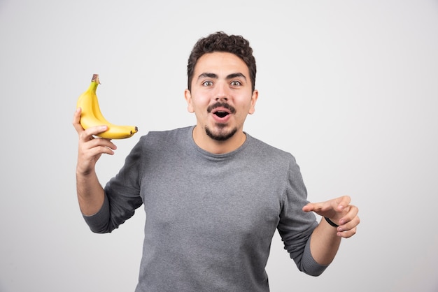 Junger Mann, der zwei reife Bananen auf Grau hält.