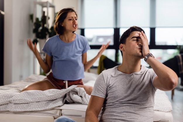 Junger Mann fühlt sich gestresst und hat Kopfschmerzen, während seine Freundin im Schlafzimmer mit ihm streitet