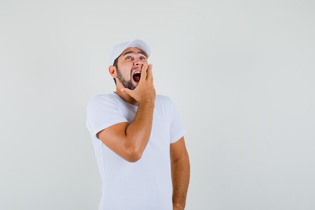 Junger Mann gähnt, während er im weißen T-Shirt aufschaut und schläfrig aussieht