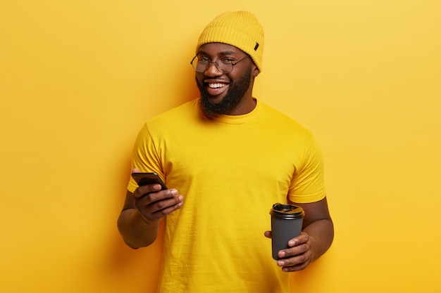Junger Mann gekleidet in gelbem Halten Telefon und Kaffeetasse