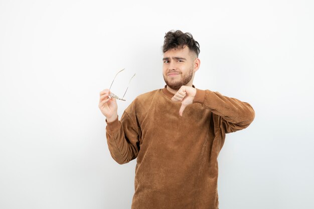 junger Mann hält Brille und zeigt Daumen nach unten.