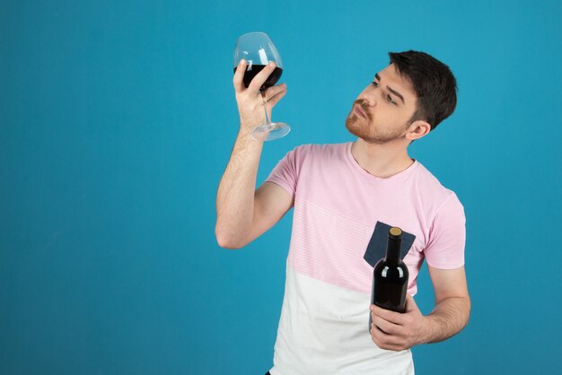 Junger Mann hält ein Glas Wein hoch und betrachtet es.