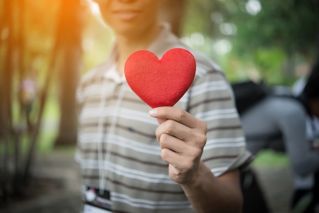 Junger Mann hält herzförmige Valentinstagkarte und schaut beim Stehen im Park.