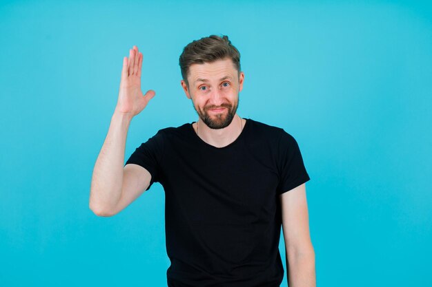 Junger Mann hebt seine linke Hand auf blauem Hintergrund