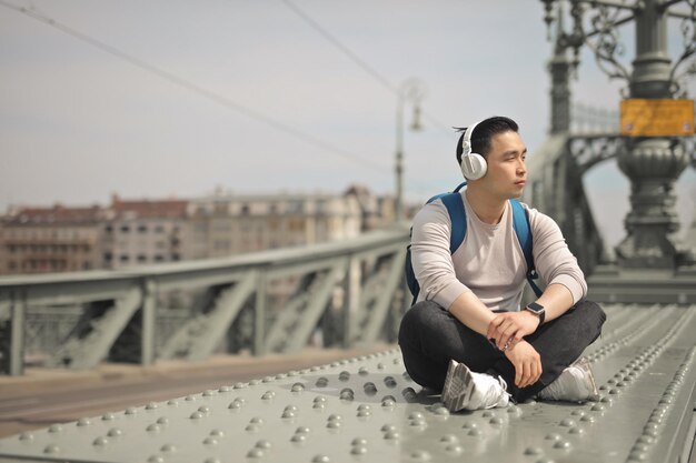 junger mann hört musik, die auf einer brücke sitzt