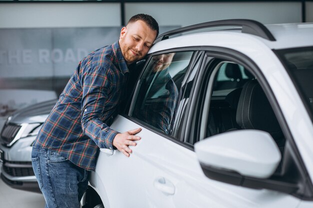 Junger Mann huggingf ein Auto in einem Autosalon