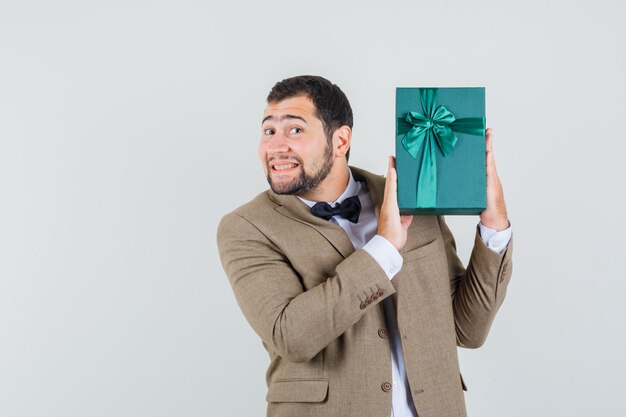 Junger Mann im Anzug hält Geschenkbox und schaut glücklich, Vorderansicht.