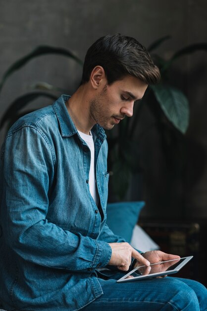 Junger Mann im blauen Denimhemd unter Verwendung der digitalen Tablette