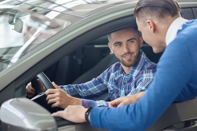 Junger Mann im blauen Pullover hilft seinem Freund bei der Auswahl des Autos