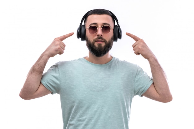 Junger Mann im blauen T-Shirt mit Bart, der Musik durch schwarze Kopfhörer hört