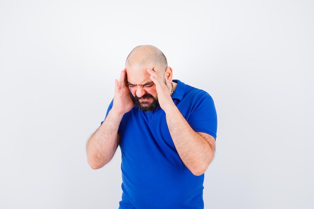 Junger Mann im blauen T-Shirt mit Kopfschmerzen