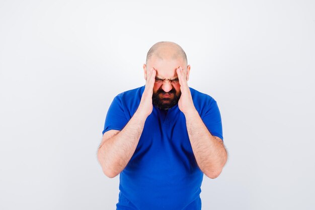 Junger Mann im blauen T-Shirt mit Kopfschmerzen