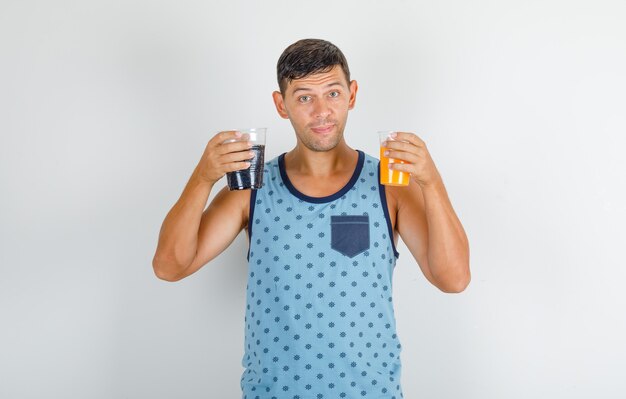 Junger Mann im blauen Unterhemd, das alkoholfreie Getränke hält