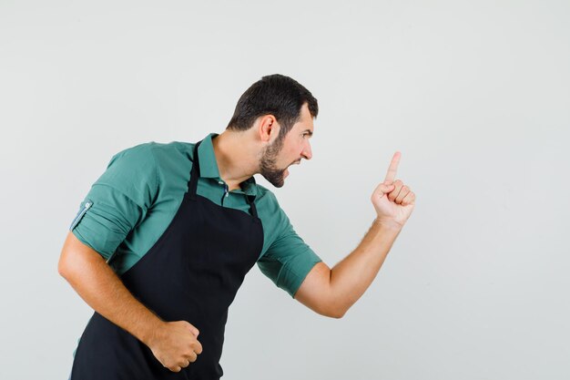 Junger Mann im grünen Hemd, der jemanden mit dem Finger warnt und wütend aussieht, Vorderansicht.