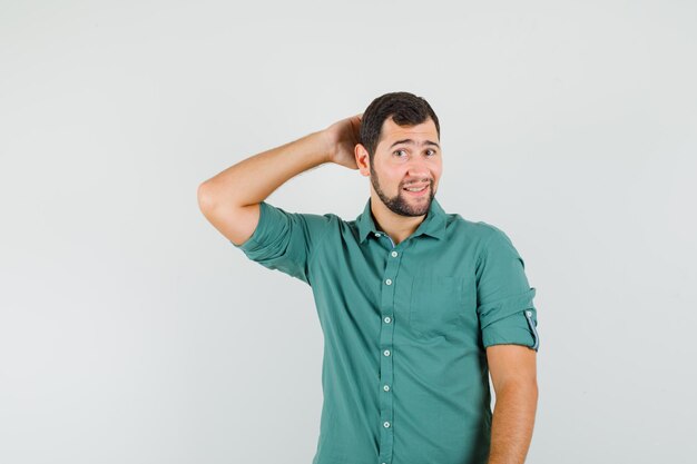 Junger Mann im grünen Hemd posiert, während er die Hand auf dem Kopf hält und gutaussehend aussieht, Vorderansicht.