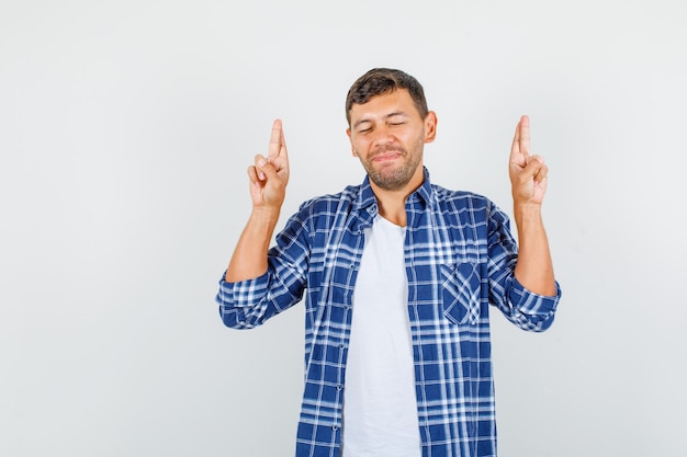 Junger Mann im Hemd, der viel Glück mit gekreuzten Fingern wünscht und hoffnungsvoll, Vorderansicht schaut.