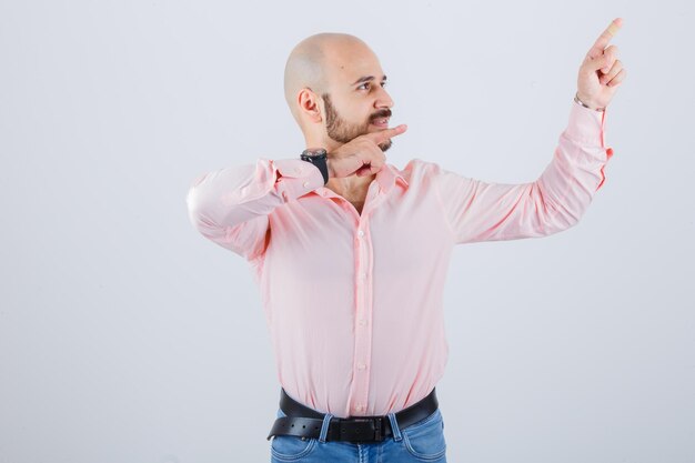 Junger Mann im Hemd, Jeans, die auf die obere rechte Ecke zeigt und selbstbewusst aussieht, Vorderansicht.