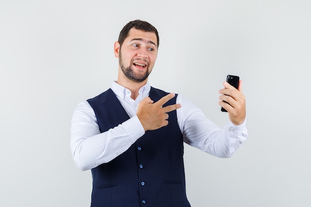 Junger Mann im Hemd, Weste, die V-Zeichen zeigt, das selfie nimmt und positiv schaut