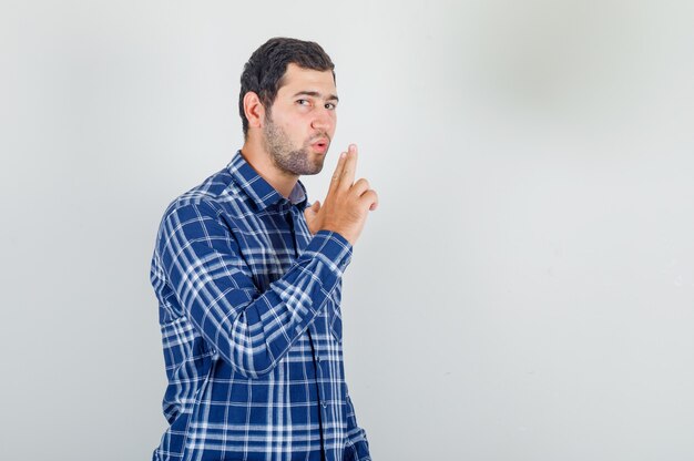 junger Mann im karierten Hemd, das auf den Fingern weht, die Waffe zeigen