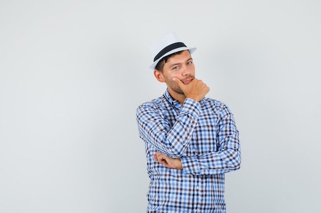 Junger Mann im karierten Hemd, Hut, der in denkender Haltung steht und optimistisch schaut