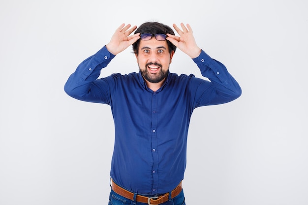 Junger Mann im königsblauen Hemd mit Brille und fröhlichem Blick, Vorderansicht.