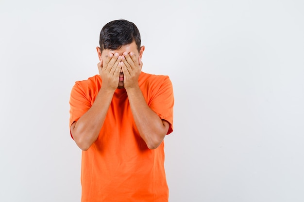 Junger Mann im orange T-Shirt, das Hände auf Gesicht hält und ängstlich schaut