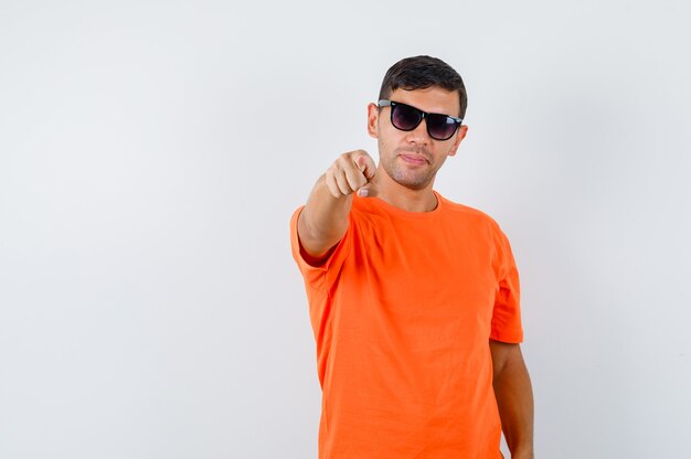 Junger Mann im orangefarbenen T-Shirt, das auf Kamera zeigt und zuversichtlich schaut