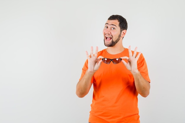 Junger Mann im orangefarbenen T-Shirt mit Sonnenbrille und fröhlichem Aussehen, Vorderansicht.