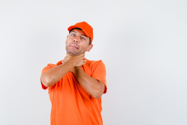 Junger Mann im orangefarbenen T-Shirt und in der Mütze, die unter Halsschmerzen leiden und krank aussehen