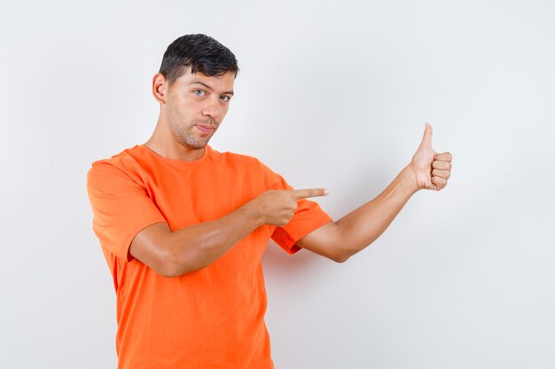 Junger Mann im orangefarbenen T-Shirt zeigt auf seinen Daumen nach oben