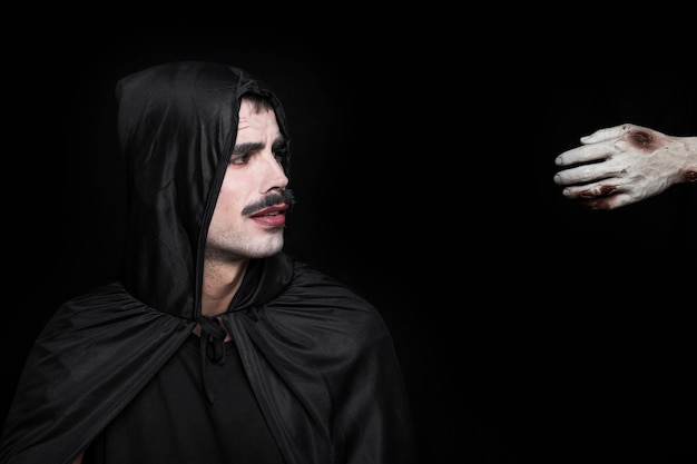 Kostenloses Foto junger mann im schwarzen halloween-kostüm und in der hand der leiche