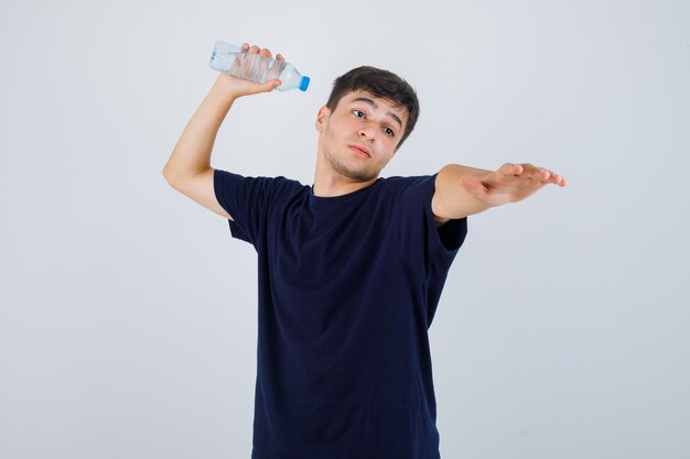 Junger Mann im schwarzen T-Shirt, das bereit ist, Flasche des Wassers wegzuwerfen und wütend, Vorderansicht zu schauen.