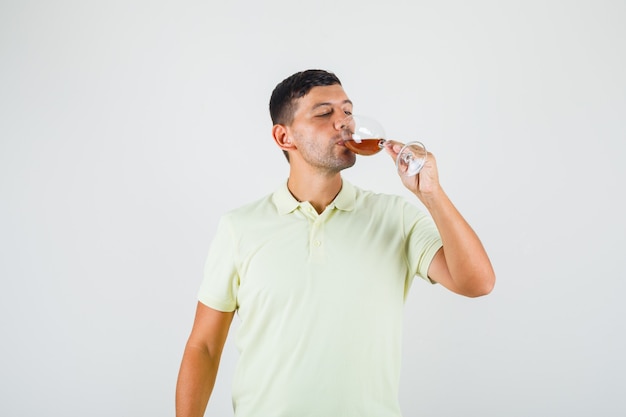 Junger Mann im T-Shirt, das Glas Alkohol trinkt.