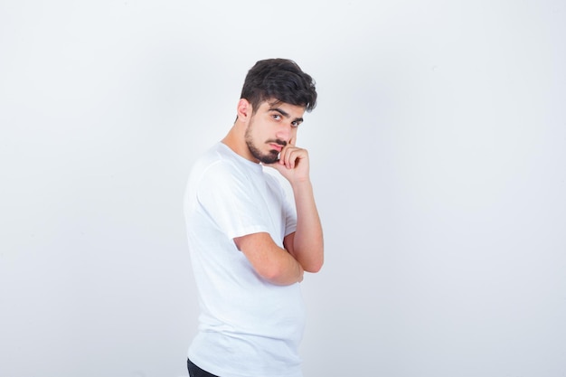 Junger Mann im T-Shirt, der in denkender Pose steht und zögerlich aussieht