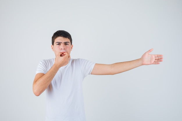 Junger Mann im T-Shirt pfeift auf Daumen und Zeigefinger und schaut selbstbewusst, Vorderansicht.