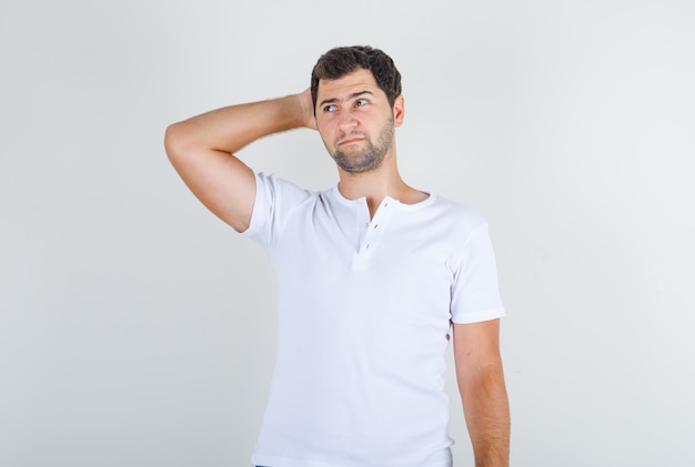 Junger Mann im weißen T-Shirt, das mit Hand hinter Kopf denkt