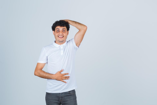 Junger Mann im weißen T-Shirt, Hose, die Hand auf dem Kopf hält und erstaunt aussieht, Vorderansicht.