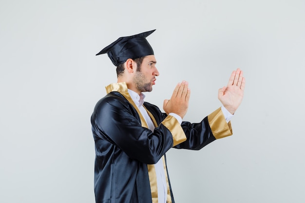 Junger Mann in der Abschlussuniform, die Karate-Hieb-Geste zeigt und boshaft aussieht.