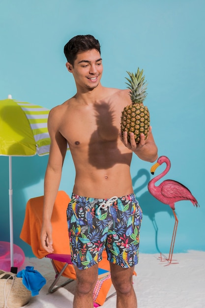 Junger Mann in der Badebekleidung, die Ananas und das Lächeln hält